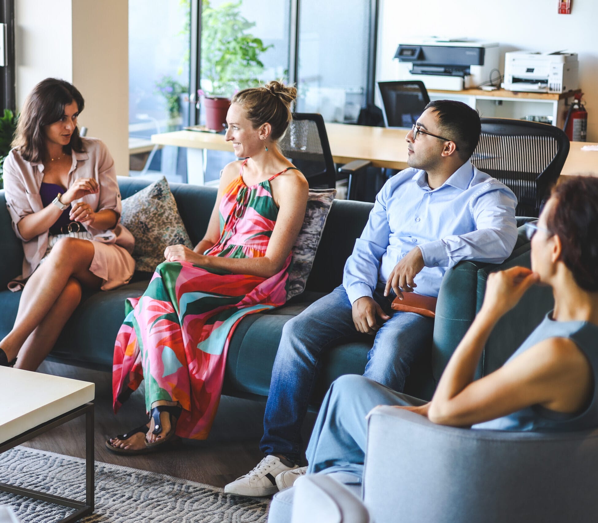 A photograph of four people sitting on couches in an office that are deep in conversation. 