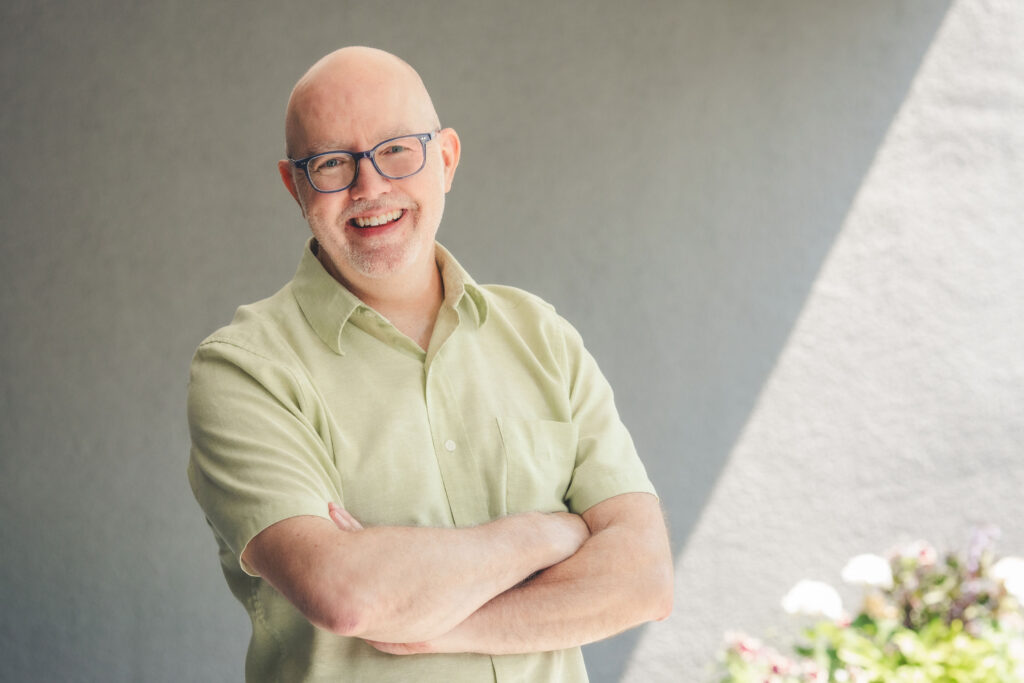 Keith Ippel, a man wearing glasses and green button-down shirt, smiles with arms crossed.