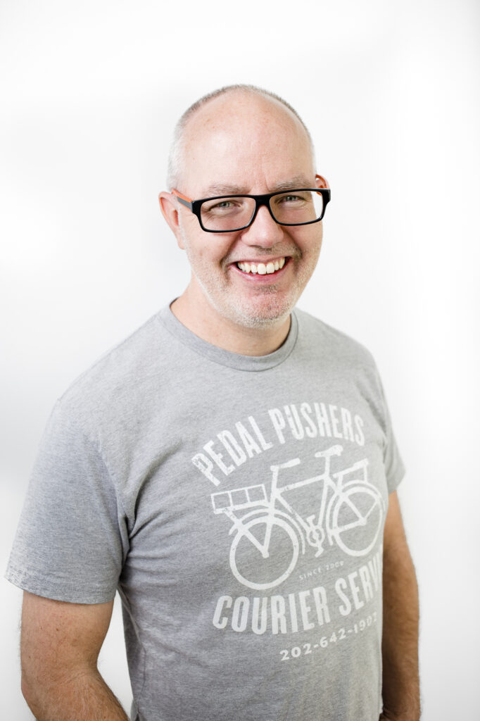Keith Ippel, a man wearing glasses and a grey t-shirt, smiles at the camera.