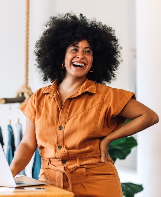 Black small business owner smiling cheerfully while standing in her shop. 